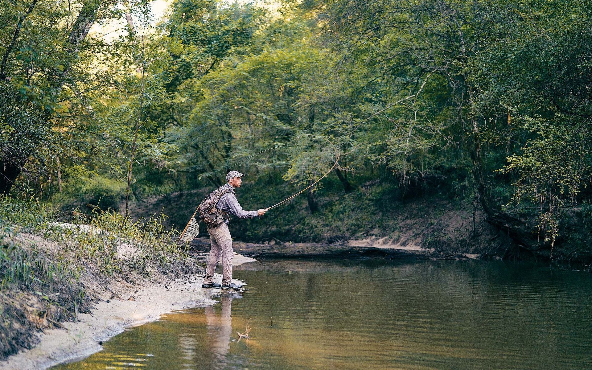 A man is fishing in a river in the woods.