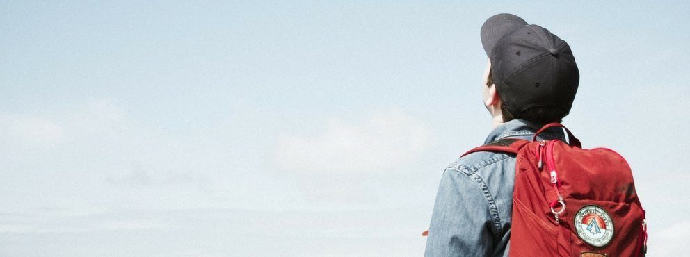 A man with a red backpack is looking at the sky.