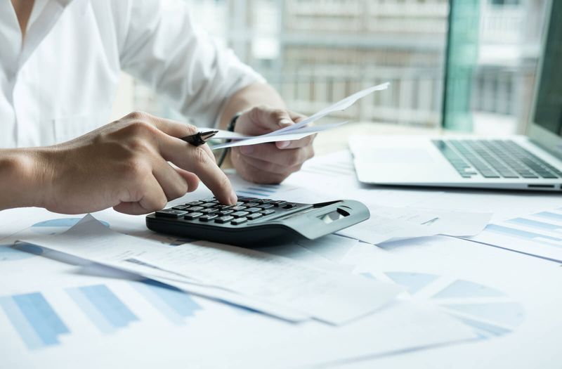 A person is using a calculator and holding a piece of paper.